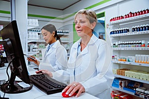 Caucasian pharmacist searching for scripts on desktop computer standing behind counter in pharmacy