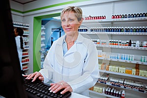 Caucasian pharmacist typing on desk top computer searching through emails standing behind counter in pharmacy