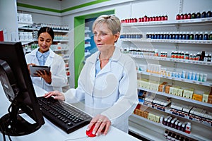 Caucasian pharmacist typing on desktop computer looking for scripts of patients standing in pharmacy