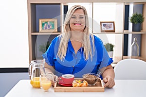 Caucasian plus size woman eating breakfast at home with a happy and cool smile on face