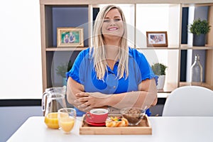 Caucasian plus size woman eating breakfast at home happy face smiling with crossed arms looking at the camera