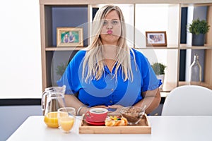 Caucasian plus size woman eating breakfast at home puffing cheeks with funny face