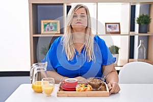 Caucasian plus size woman eating breakfast at home relaxed with serious expression on face
