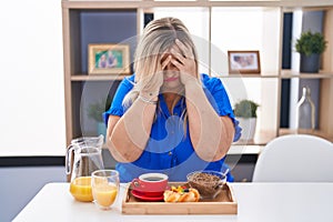Caucasian plus size woman eating breakfast at home with sad expression covering face with hands while crying