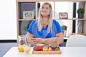 Caucasian plus size woman eating breakfast at home smiling looking to the side and staring away thinking