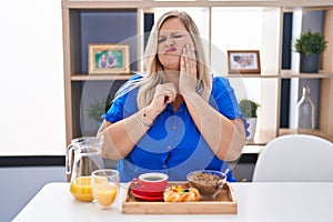Caucasian plus size woman eating breakfast at home touching mouth with hand with painful expression because of toothache or dental