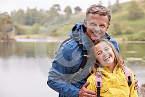Caucasian pre-teen girl standing with her father on the shore of a lake, laughing at camera, close up