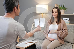 Caucasian pregnant female communicating with professional psychologist man psychotherapist showing pictures for examining mental