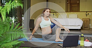 Caucasian pregnant woman practicing yoga at home with online lessons