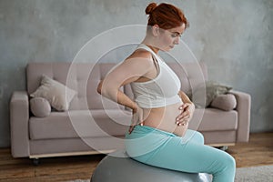Caucasian pregnant woman suffers from belly pain. Fitball training during pregnancy.