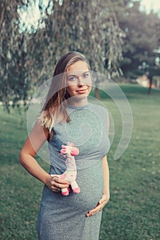 Caucasian pregnant woman touching her belly and holding pink stuffed plush toy giraffe.
