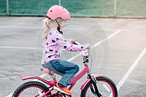 Caucasian preschooler girl riding pink bike bicycle in helmet on backyard road outside on spring summer day.