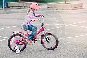 Caucasian preschooler girl riding pink bike bicycle in helmet on backyard road outside on spring summer day.