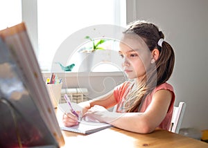 Caucasian preteen girl concentrated on her task with schoolbook. Concept of distance learning in isolation while coronavirus