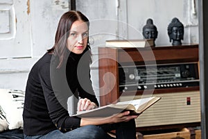 Caucasian pretty brunette woman sitting with a book indoors. Con