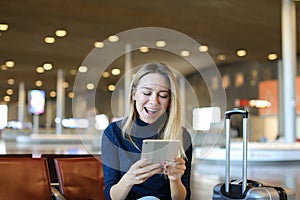 Caucasian pretty woman sitting in airport waiting room with valise and using tablet.