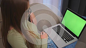 Caucasian pretty young woman using laptop with green screen, sitting on the couch sofa at the home. Chromakey.