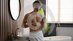 Caucasian relaxed man in bathroom calm male naked guy with towel on hips in bathroom drinking coffee holding cup of tea