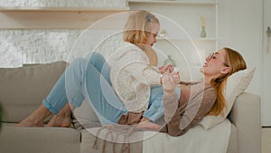 Caucasian relaxed mother and cute small child daughter talking friendly speaking conversation talk lying on sofa smiling