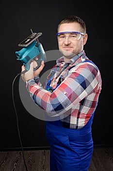 Caucasian repairman in goggles holding woodworking tools. Carpenter portrait on black studio background