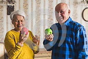 Caucasian retired grandmother and grandfather in an old fashioned apartment holding fresh red and green apples. Healthy