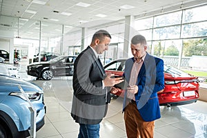 Caucasian salesman holding clipboard and talking about buying car with sale with his customer