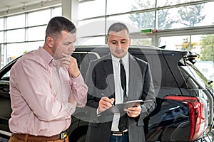 Caucasian salesman holding clipboard and talking about buying car with sale with his customer