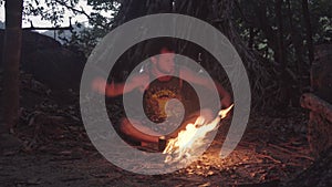 Caucasian Savage Man Burning Little Campfire in the Tropical Forest at Twilight to Boil Kettle with Rice for Dinner