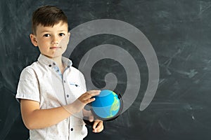 Caucasian schoolboy at a geography lesson stands near the blackboard in the classroom. schoolboy or college student with