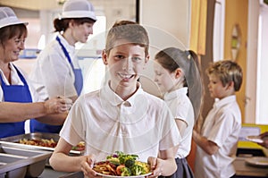 Caucasian schoolboy holds plate of food in school cafeteria