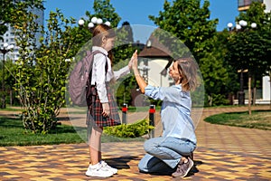 Caucasian schoolgirl with backpack and uniform says goodbye to her mother