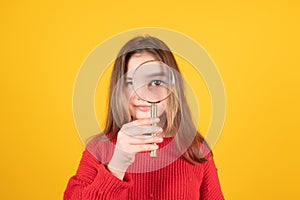 Caucasian schoolgirl looking through the magnifying glass. Teen girl in red sweater on yellow background.