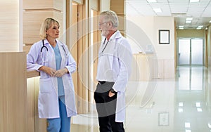 Caucasian senior beard male and female doctors wearing white gown uniforms with stethoscope, consulting, talking to each other in