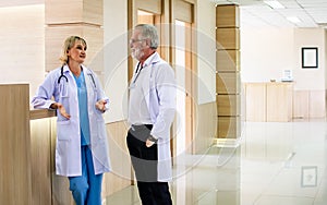 Caucasian senior beard male and female doctors wearing white gown uniforms with stethoscope, consulting, talking to each other in