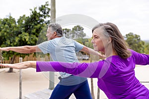 Caucasian senior couple with arms outstretched practicing warrior 2 yoga pose at beach