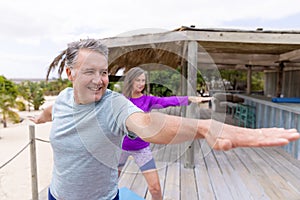 Caucasian senior couple with arms outstretched practicing warrior 2 yoga pose at tourist resort