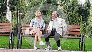 Caucasian senior couple in casual clothes sitting on bench and talking with wooman in park