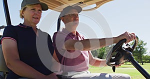 Caucasian senior couple driving a golf cart with clubs on the back at golf course