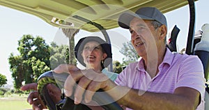 Caucasian senior couple driving a golf cart with clubs on the back at golf course