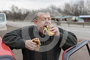 Caucasian senior driver gobbling lyulya kebab in lavash near his car