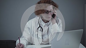 Caucasian senior female doctor physician talking on mobile at work. Healthcare professional answering call giving remote