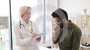 Caucasian senior female doctor and young male patient sitting at exam couch.