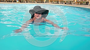 Caucasian senior female elderly in a hat swims in a blue water pool in a hotel. The concept of a healthy lifestyle