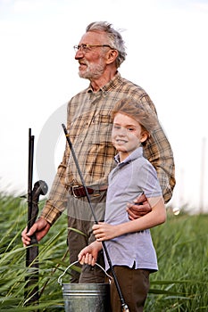 Caucasian senior fisherman hugging little grandson while fishing together on lake