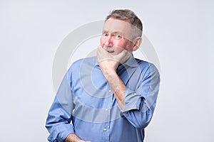 Caucasian senior grandfather curves lips, looks doubtfully, thinks what to do.