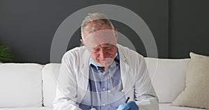 Caucasian senior male doctor with lowered face mask taking notes while having a video call