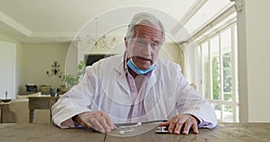Caucasian senior male doctor wearing lab coat sitting at table talking, giving video consultation