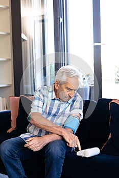 Caucasian senior man checking his blood pressure sitting on the couch at home