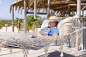 Caucasian senior man with hat on face sleeping on hammock at beach during sunny day