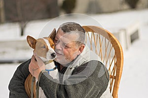 Caucasian senior man with his cute basenji dog sitting in wicker chair at sunny winter day